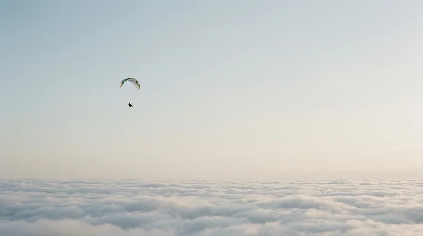 A lone paraglider high above a sea of cloud.
